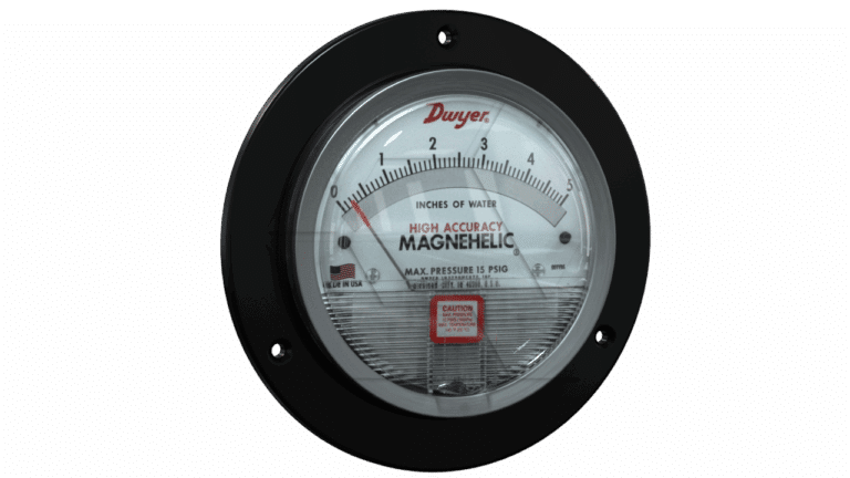 A round, black-framed Magnehelic gauge by Dwyer measures pressure in inches of water, with a clear front, labeled dial, and a needle pointing just above zero. The face displays warnings and the U.S. flag.